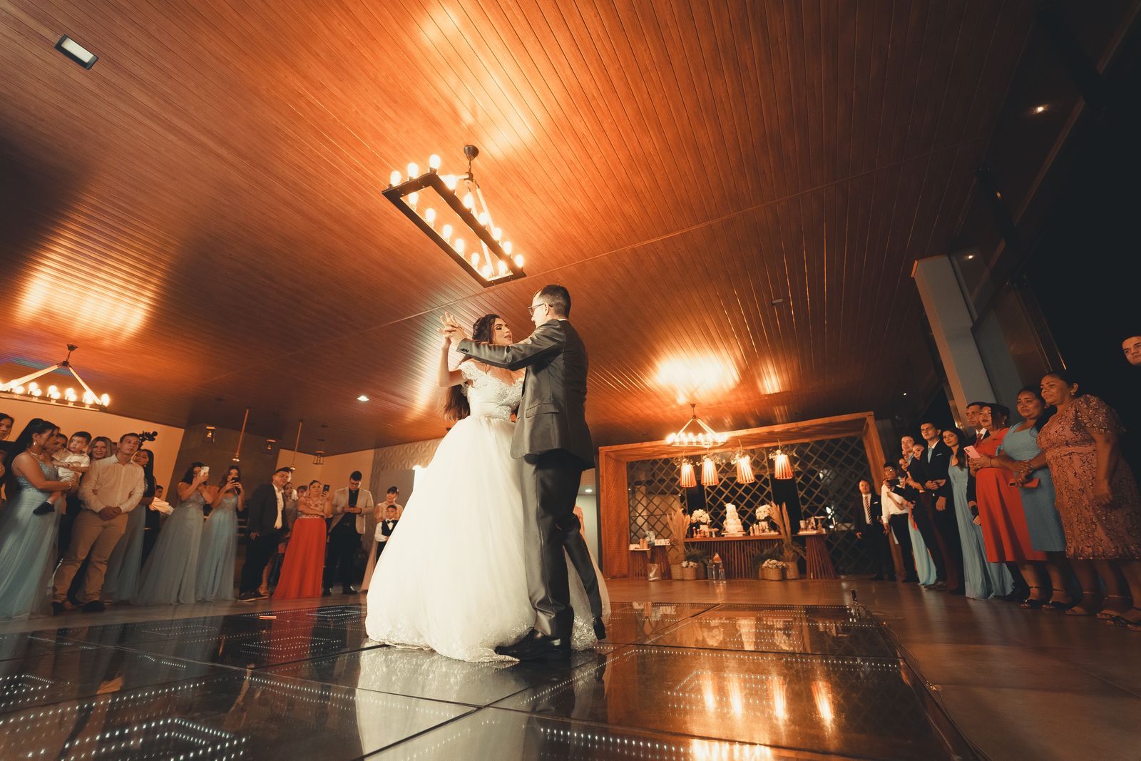 Bride and groom sharing a first dance while guests watch and film