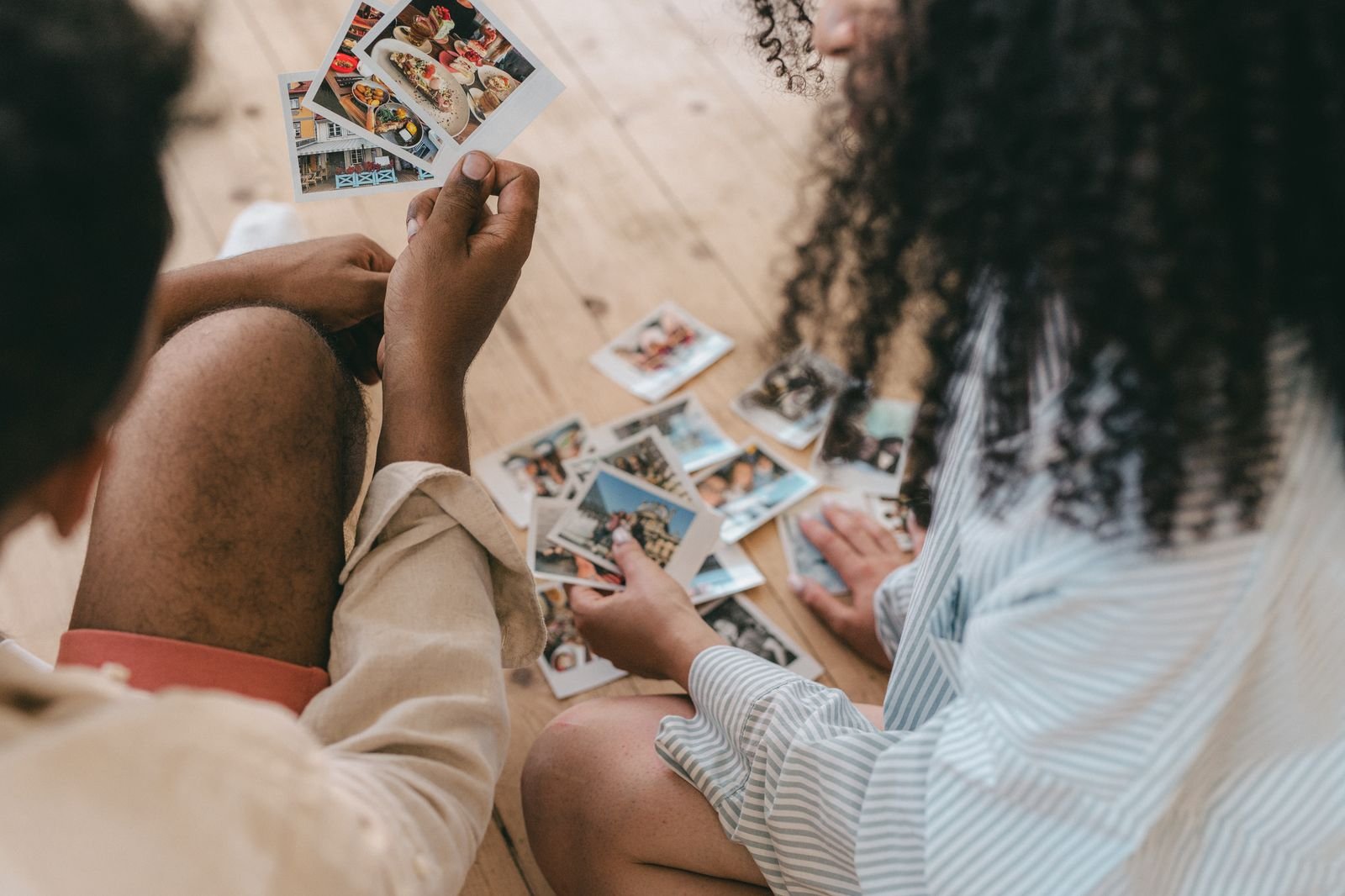 Couple sitting on a wooden floor sorting through printed photographs together